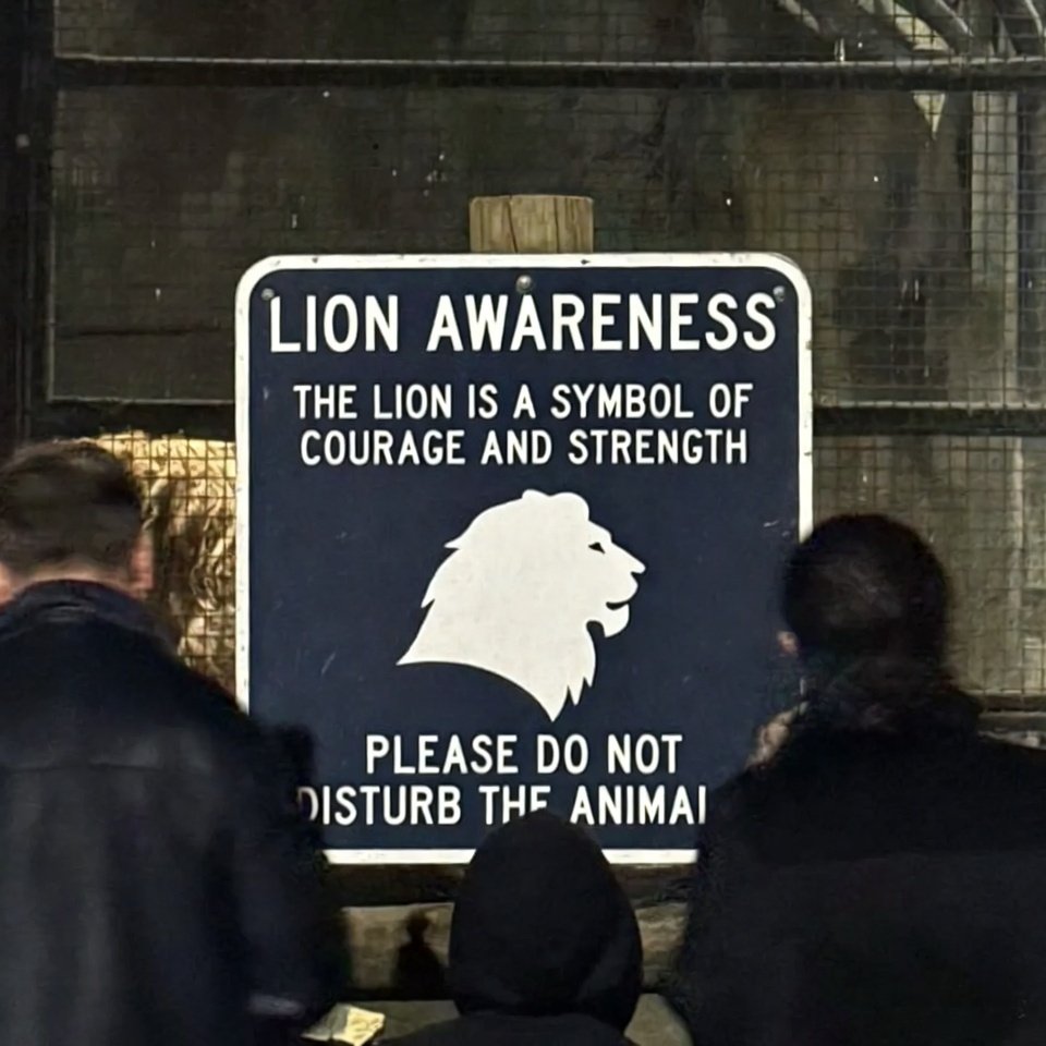 Grainy side-angle shot of lion awareness sign at zoo.