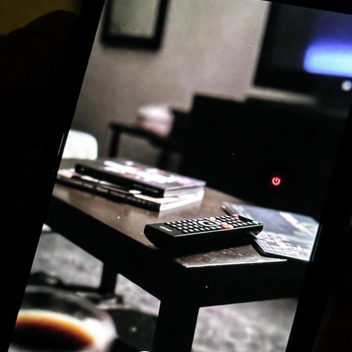 Hand holding tilted phone showing dark living room TV setup Hand holding tilted phone showing dark living room TV setup